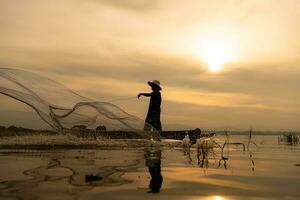 Silhouette of fisherman at sunrise, Standing aboard a rowing boat and casting a net to catch fish for food photo