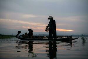 Silhouette of fisherman at sunrise, Standing aboard a rowing boat and casting a net to catch fish for food photo