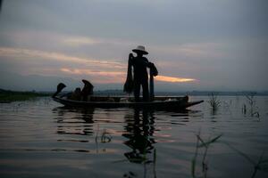 Silhouette of fisherman at sunrise, Standing aboard a rowing boat and casting a net to catch fish for food photo