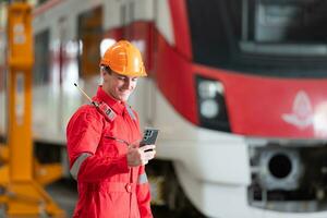 Portrait of a technician using a mobile phone in front of a train while relaxing after inspecting the electric train's machinery repairs. photo