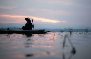Silhouette of fisherman at sunrise, Standing aboard a rowing boat and casting a net to catch fish for food photo