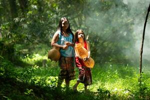 Two girls Asian women with traditional clothing stand in the rainforest. They had fun playing together before assisting Grandpa in catching fish in a nearby lake. photo