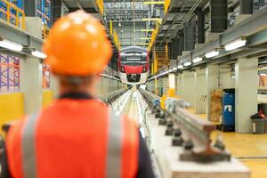 posterior ver de eléctrico tren industria ingeniero vistiendo un la seguridad casco y reflexivo chaleco. allí es un eléctrico coche en el coche reparar fábrica como el antecedentes imagen. foto