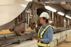 eléctrico tren ingeniero inspeccionar eléctrico tren maquinaria con tabletas según a inspección redondo después el eléctrico tren es estacionado en el eléctrico tren reparar tienda foto