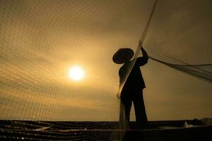 silueta de pescador a amanecer, en pie a bordo un remo barco y fundición un red a captura pescado para comida foto