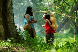 Two girls Asian women with traditional clothing stand in the rainforest. They had fun playing together before assisting Grandpa in catching fish in a nearby lake. photo