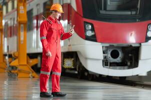 Portrait of a technician using a mobile phone in front of a train while relaxing after inspecting the electric train's machinery repairs. photo