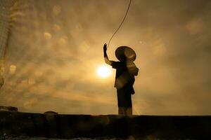 Silhouette of fisherman at sunrise, Standing aboard a rowing boat and casting a net to catch fish for food photo