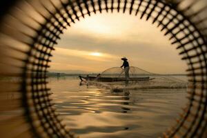 silueta de pescador a amanecer, en pie a bordo un remo barco y fundición un red a captura pescado para comida foto