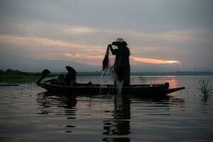 Silhouette of fisherman at sunrise, Standing aboard a rowing boat and casting a net to catch fish for food photo