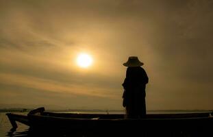 Silhouette of fisherman at sunrise, Standing aboard a rowing boat and casting a net to catch fish for food photo