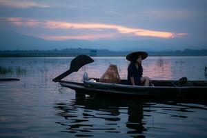 Silhouette of fisherman at sunrise, Standing aboard a rowing boat and casting a net to catch fish for food photo