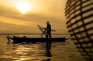 silueta de pescador a amanecer, en pie a bordo un remo barco y fundición un red a captura pescado para comida foto