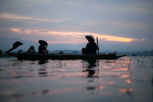 Silhouette of fisherman at sunrise, Standing aboard a rowing boat and casting a net to catch fish for food photo