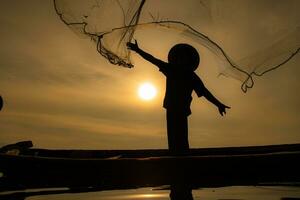 Silhouette of fisherman at sunrise, Standing aboard a rowing boat and casting a net to catch fish for food photo