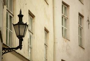 An old dark street lamp with glass inserts hangs on the wall of a house in Tallinn. High quality photo