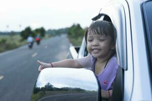 Cheerful girl waving out of car window,Little girl on vacation traveling by car, beautiful landscape. photo