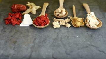 Spoon of dry chinese herbs arrange in row on black photo