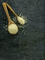 Top view of white sesame seeds on wooden spoon against black photo