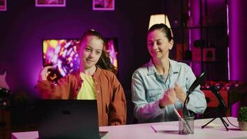 joven niña enseñando su madre cómo a hacer viral en línea danza se mueve mientras rodaje vídeo para Internet canal. padre aprendizaje tendencias coreografía desde hija en hogar estudio iluminado por rosado neón video