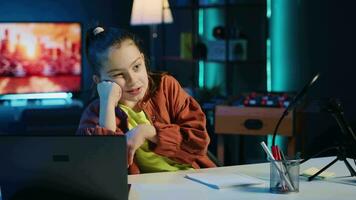 Upset child filming family vlog in home studio, talking about annoying school homework for her children audience. Young girl recording content for social media, discussing with gen Z fans video