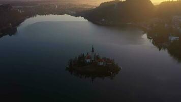 blödde sjö och marijinega vnebovzetja kyrka på soluppgång. gyllene timme. kullar och skog. Slovenien, Europa. reflexion i sjö. antenn se. Drönare flugor bakåt, luta upp. avslöja skott video