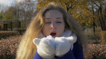 jovem lindo caucasiano mulher dentro branco luvas é sopro neve dentro inverno dentro ensolarado dia. lento movimento. video