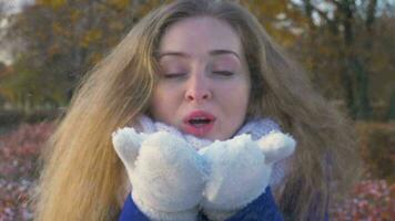 jovem lindo caucasiano mulher dentro branco luvas é sopro neve dentro inverno dentro ensolarado dia. video