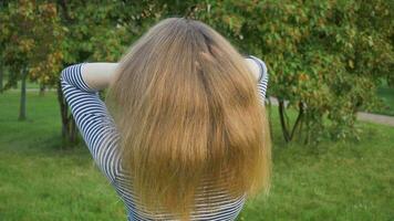 jong blond vrouw is het werpen omhoog haar gezond lang haren door handen in groen park. super langzaam beweging. video