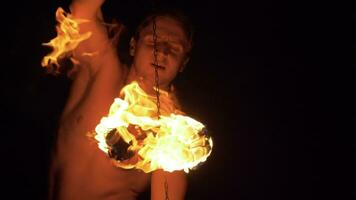 hombre con muscular cuerpo es ejecutando fuego espectáculo. dos bolas de fuego en cadenas son hilado alrededor. súper lento movimiento. video