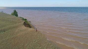 Young athletic woman is walking along the precipitous coastline of sea. Aerial view. video