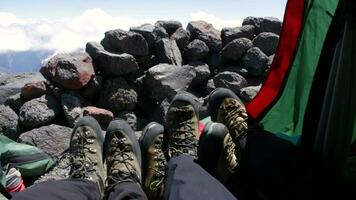 Mountaineers in black pants and mountain boots are lying in tent and shaking by their legs. Stone wall is on background. video