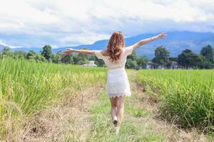 Behind scenes of a beautiful female tourist having fun walking through the bright green rice fields in the rainy season and the beautiful rice fields still being grown organically. Copy Space for text photo