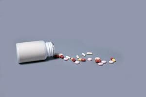 Pills spilling out of pill bottle white and two-colored capsules pills  Medicines and prescription pills flat lay background. White medical pills and tablets spilling out of a drug bottle. photo