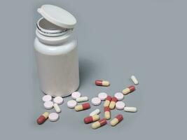 Pills spilling out of pill bottle white and two-colored capsules pills  Medicines and prescription pills flat lay background. White medical pills and tablets spilling out of a drug bottle. photo