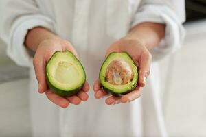 Closeup woman hands holding out at camera halves of ripe organic avocado fruit. Healthy eating, vegetarianism, dieting photo