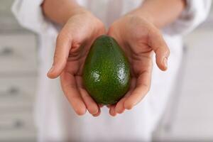 Closeup woman hands holding out at camera a fresh ripe organic avocado fruit. Healthy eating, vegetarianism, dieting photo