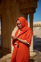 Beautiful Middle Eastern woman with head covered in hijab, praying with her hands cupped near marble wall of a mosque photo