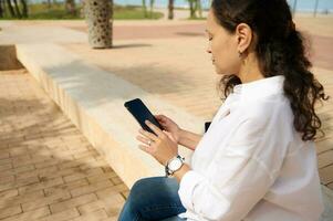 Rear view of business woman in white shirt, using smartphone and tapping screen while chatting online, booking, ordering photo