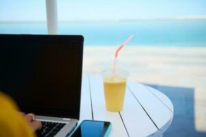 Selective focus. Partial view laptop and smart mobile phone with mockup digital screen and glass of fresh fruit smoothie photo