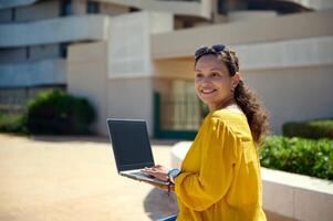 Smiling middle aged confident business woman using a laptop with black blank mockup screen. Copy space for mobile app photo