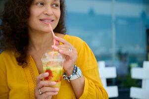 Close-up young adult multi-ethnic woman drinking fresh juice outdoor, pensively looking aside a copy advertising space photo