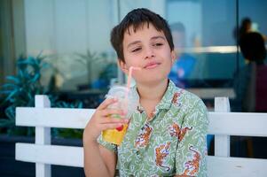 Handsome teen boy in summer shirt, holding a glass of freshy squeezed orange juice, thoughtfully looking aside photo