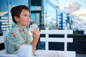 Adorable Hispanic teenage boy drinking healthy smoothie, sitting on a cafe outdoor photo