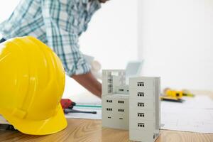 architect is preparing house model and construction plans on blueprints for construction engineering team to review before construction engineering team constructs building according to the drawings. photo