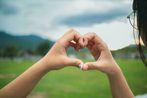 joven mujer y su amigo elevado su manos juntos a formar corazón forma a espectáculo su amistad amor y amabilidad con su creencia y poder de fe en su amistad. concepto de amistad foto