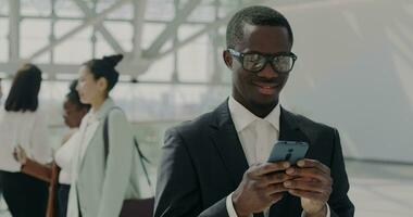 lento movimento retrato do atraente africano americano Gerente dentro terno usando Smartphone digitando dentro Inovativa escritório salão. comunicação e tecnologia conceito. video