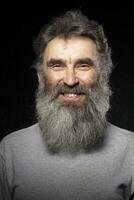 The face of an elderly smiling man with a gray beard on a black background. photo