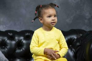 Little African American girl in bright yellow clothes at home. photo