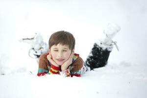 A funny little boy in colorful clothes lies in the snow. A hardened child in winter. photo